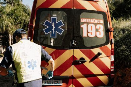 Profissional de emergência ao lado de uma ambulância em uma via urbana brasileira.