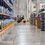 Empilhadeira movimenta mercadorias em um armazém industrial com produtos empilhados.