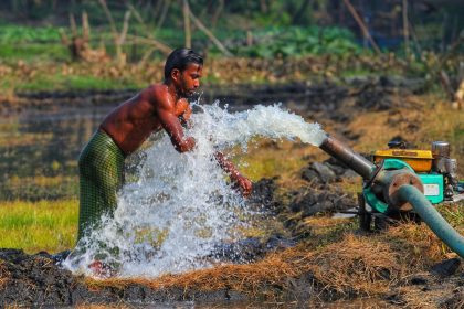 Homem opera uma bomba d’água para irrigar uma plantação em área rural.
