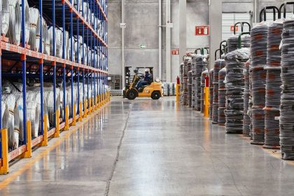 Empilhadeira movimenta mercadorias em um armazém industrial com produtos empilhados.