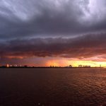 Horizonte urbano de Porto Alegre sob um céu escuro e carregado, com luzes do pôr do sol entre as nuvens.