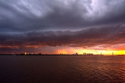 Horizonte urbano de Porto Alegre sob um céu escuro e carregado, com luzes do pôr do sol entre as nuvens.