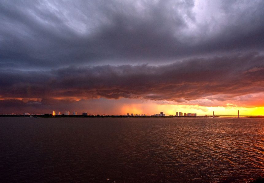 Horizonte urbano de Porto Alegre sob um céu escuro e carregado, com luzes do pôr do sol entre as nuvens.