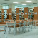 Interior amplo de uma biblioteca, com estantes de livros e mesas organizadas para estudo e leitura
