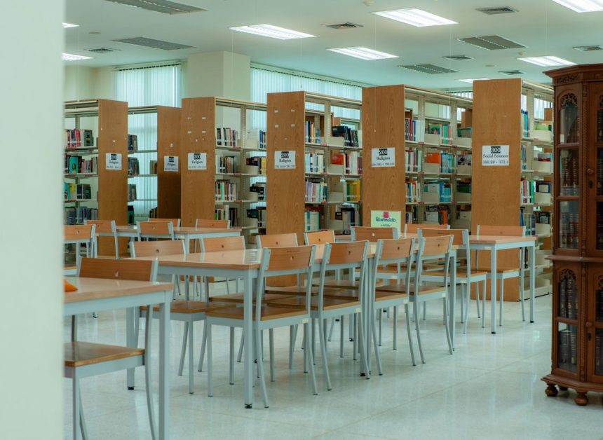 Interior amplo de uma biblioteca, com estantes de livros e mesas organizadas para estudo e leitura
